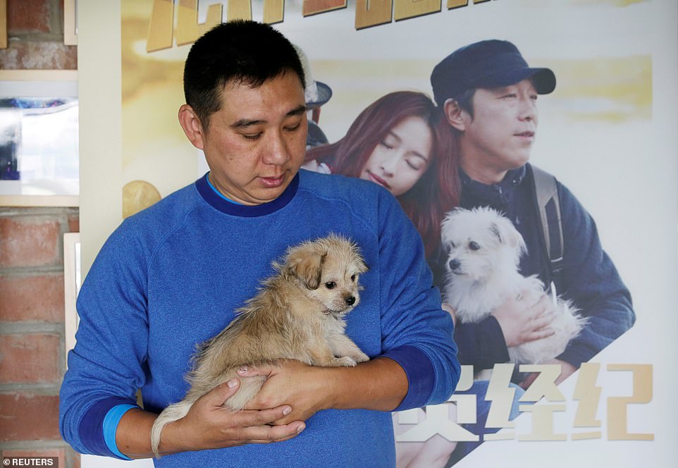 He Jun, the owner of 'Juice', poses with two-month-old 'Little Juice'  next to a film poster which shows its source dog